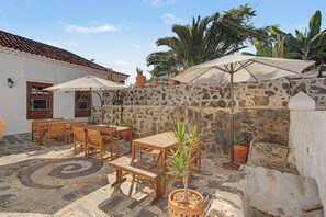 An outdoor patio with wooden furniture, stone walls, and potted plants. - Vacation Apartment 'Roja' with Mountain View, Wi-Fi and Air Conditioning (La Laguna)