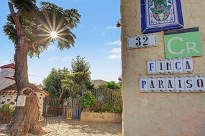 Une scène de rue avec un arbre, une clôture et un bâtiment dont le mur est recouvert de carreaux et sur lequel on peut voir des enseignes.