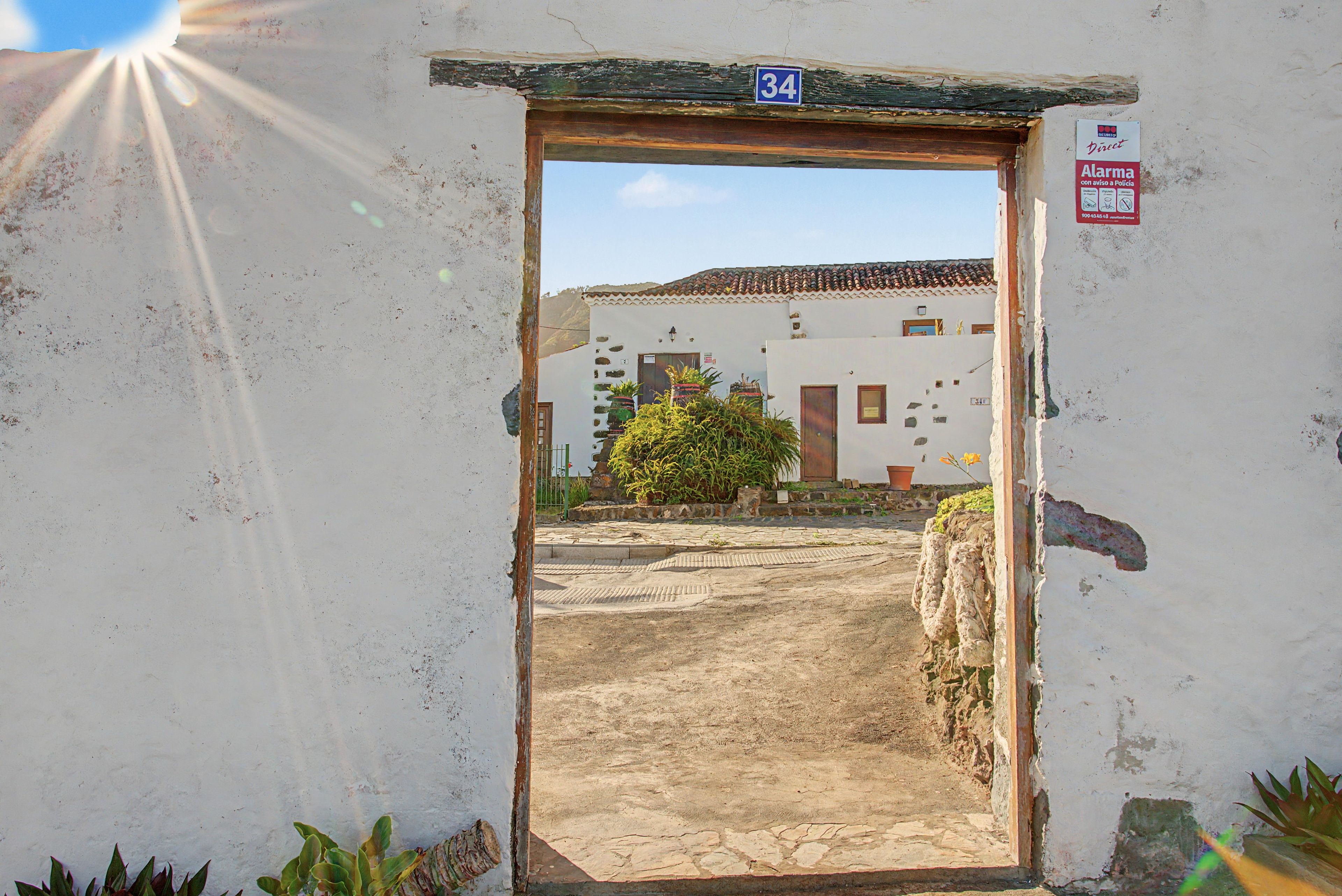 Un acceso con cartel de número, que lleva a un edificio con techo de tejas y un pequeño jardín.