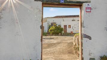 Un acceso con cartel de número, que lleva a un edificio con techo de tejas y un pequeño jardín.