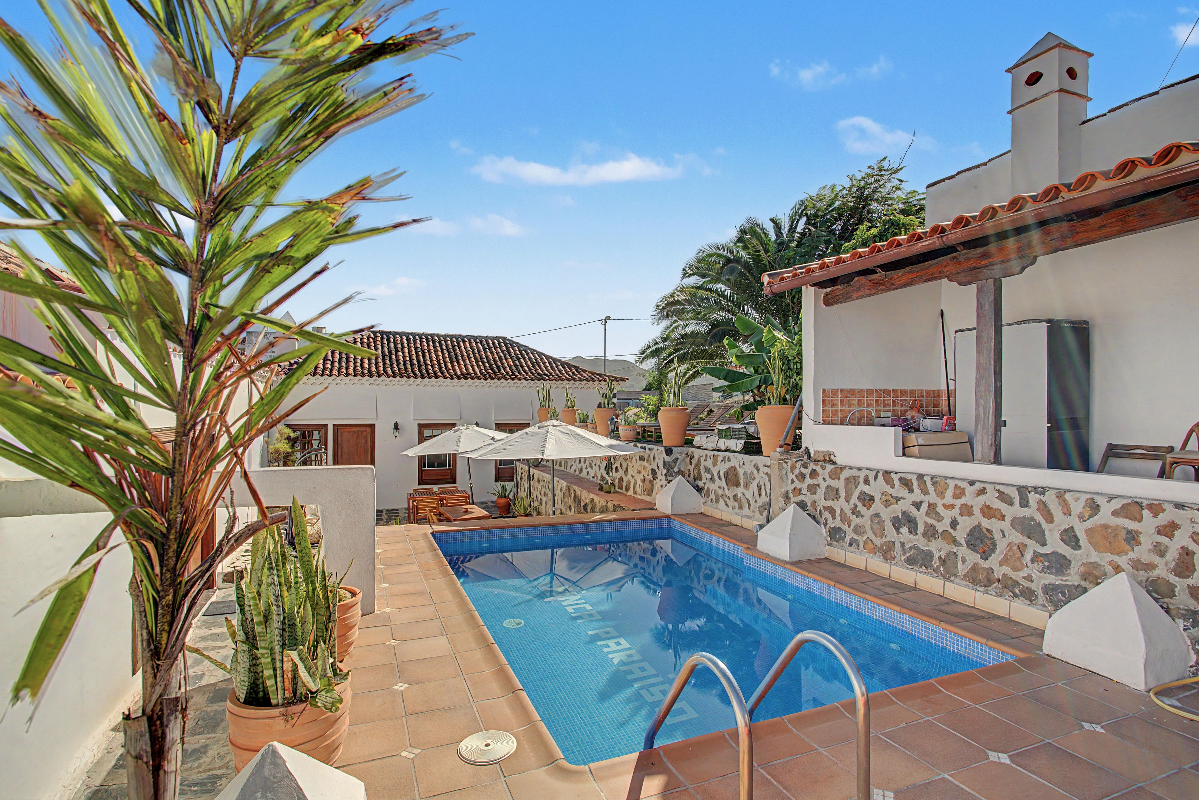 Piscina con muro de piedra, terraza de madera y mobiliario exterior.