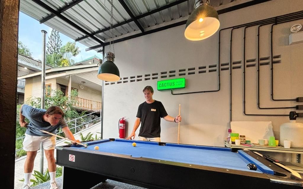 A pool table with a cue ball and a billiard cue, a person playing, and a sign that reads 'CACTUS.'