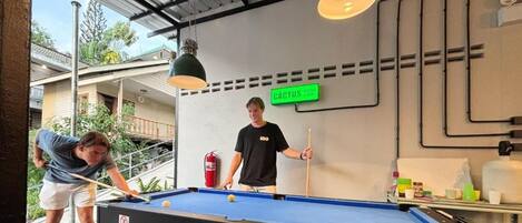 A pool table with a cue ball and a billiard cue, a person playing, and a sign that reads 'CACTUS.'