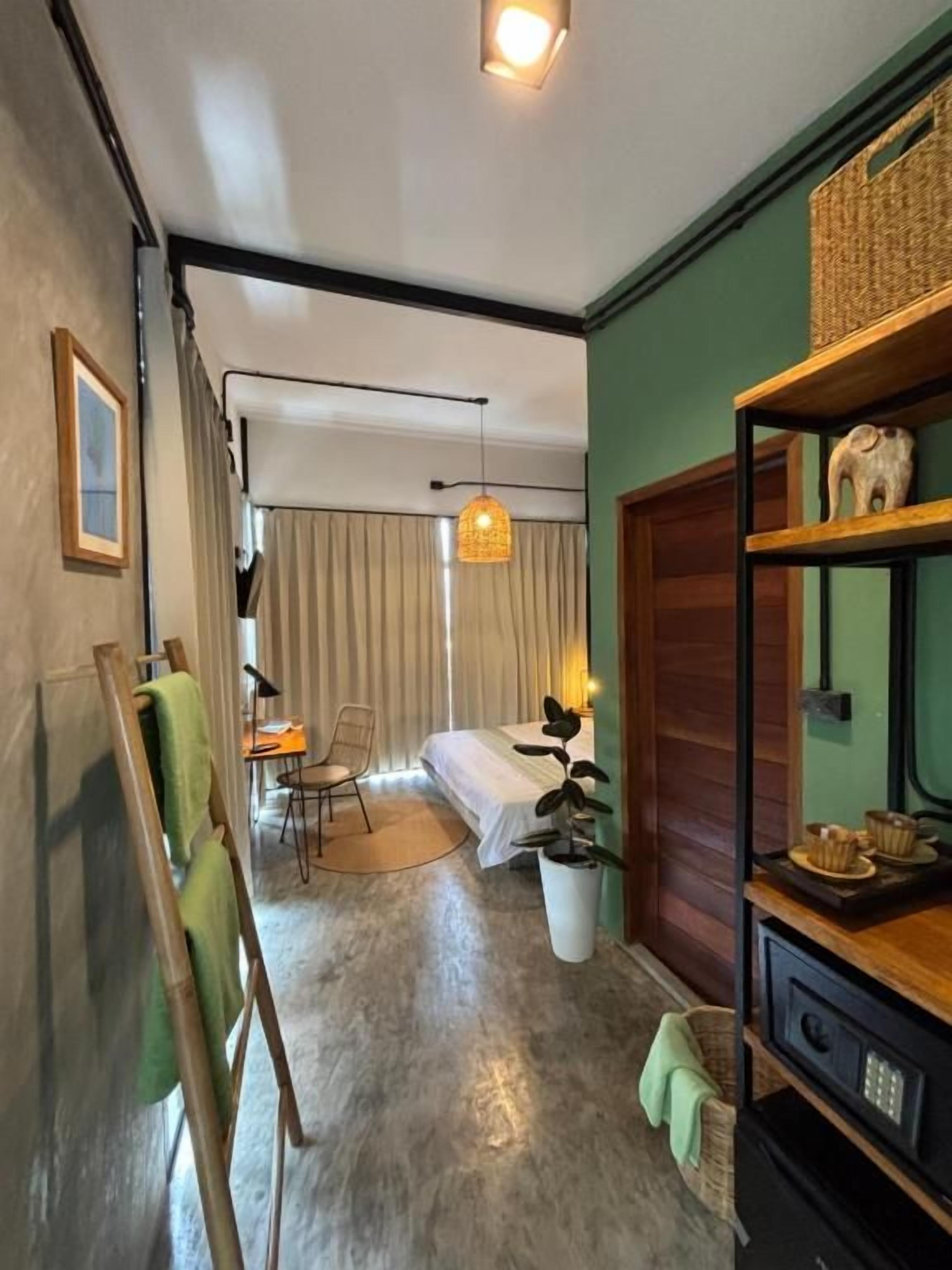 Een kamer met een bed, een bureau, een stoel, een kamerplant en een plank met decoratieve spullen.