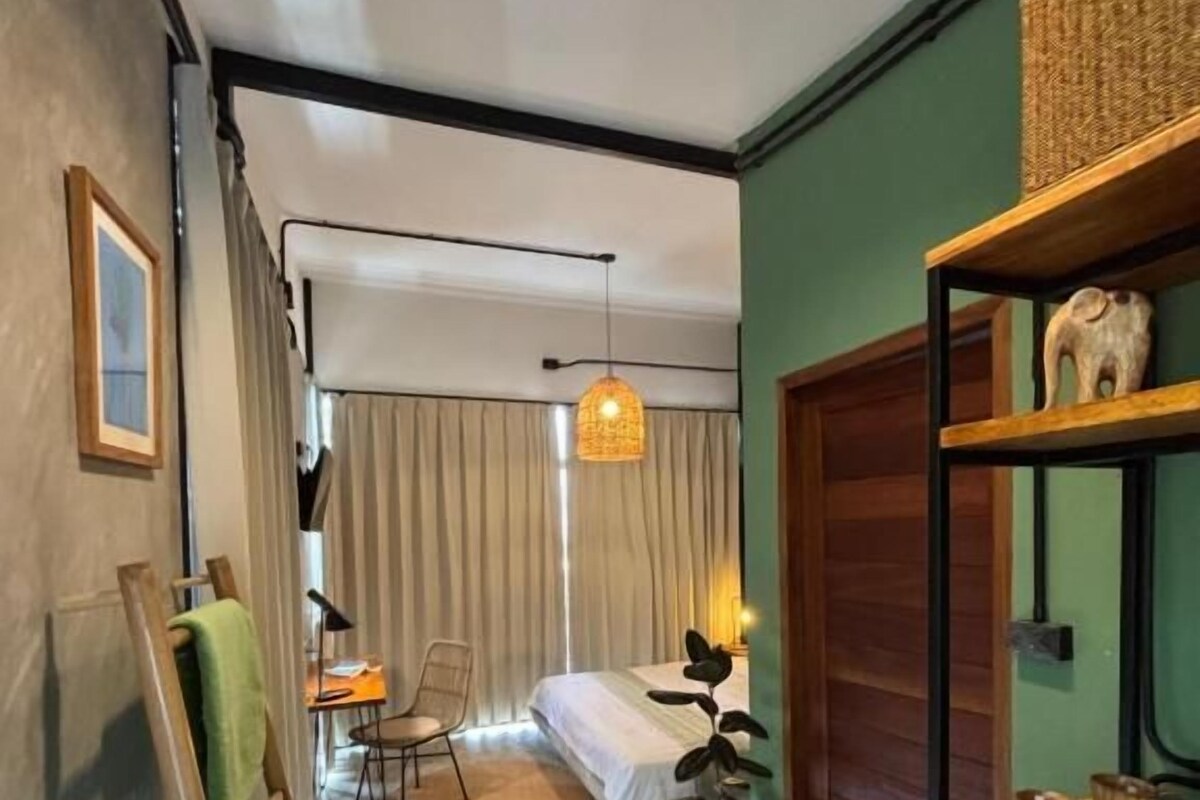 Ein Zimmer mit einem Bett, einem Schreibtisch, einem Stuhl, einer Zimmerpflanze und einem Regal mit Dekoration.