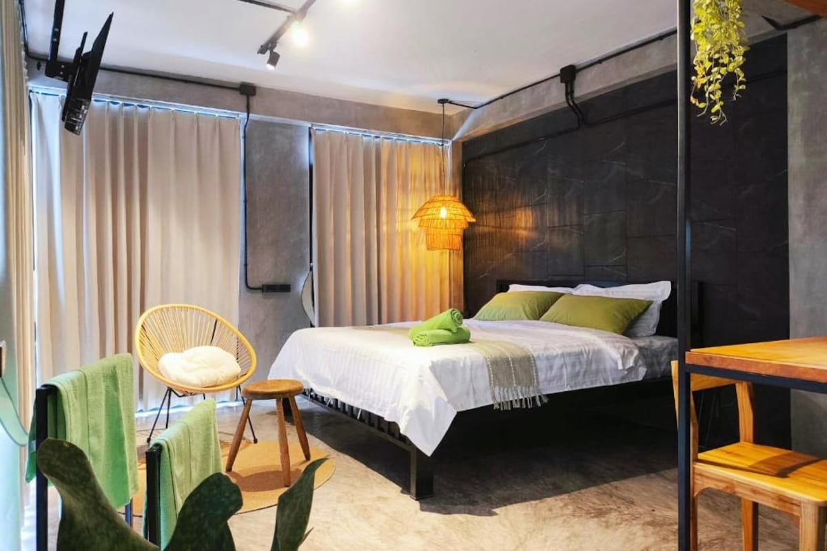 Ein modernes Schlafzimmer mit einem Bett, einem Sessel, einem Tisch und einer hängenden Pflanze.
