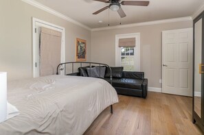 Une chambre à coucher avec un lit, un canapé en cuir noir, un ventilateur de plafond et une porte.