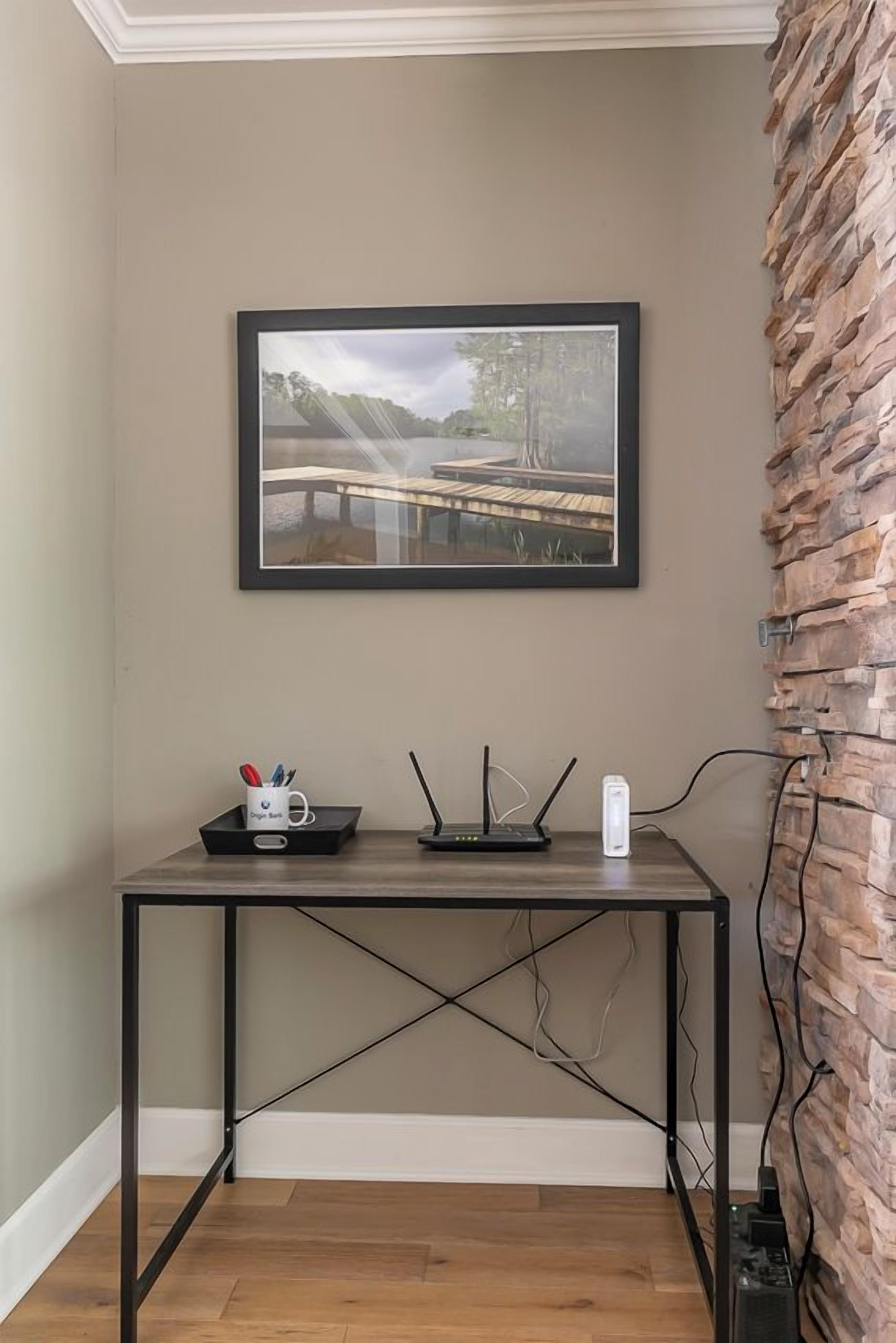 Een kamer met een lijst met een foto van een brug, een bureau met een router en een mok, en een bakstenen muur.