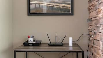 Een kamer met een lijst met een foto van een brug, een bureau met een router en een mok, en een bakstenen muur.