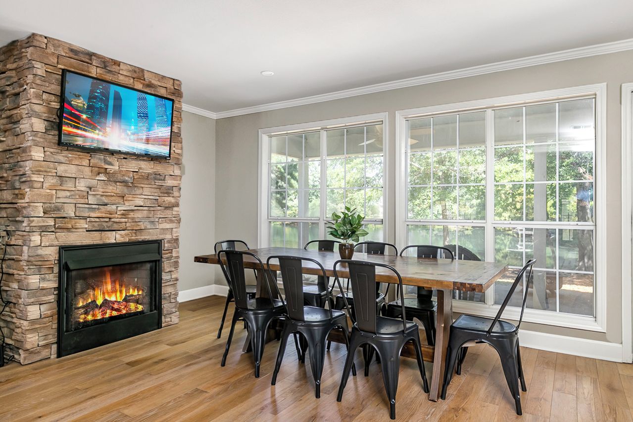 A dining area with a stone fireplace, a television mounted on the wall, and large windows.
