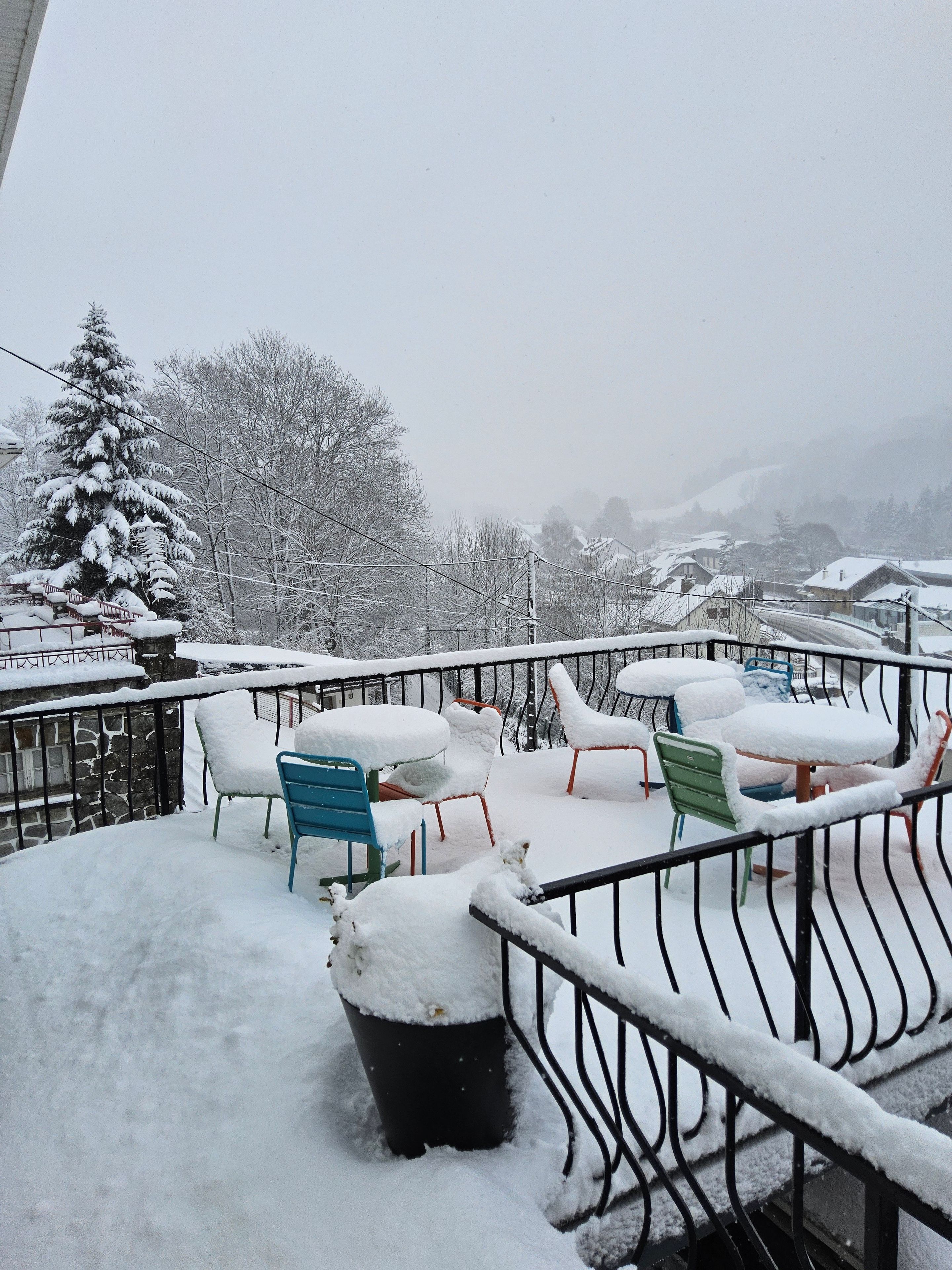 A snow-covered balcony with outdoor furniture and a view of a snowy landscape.