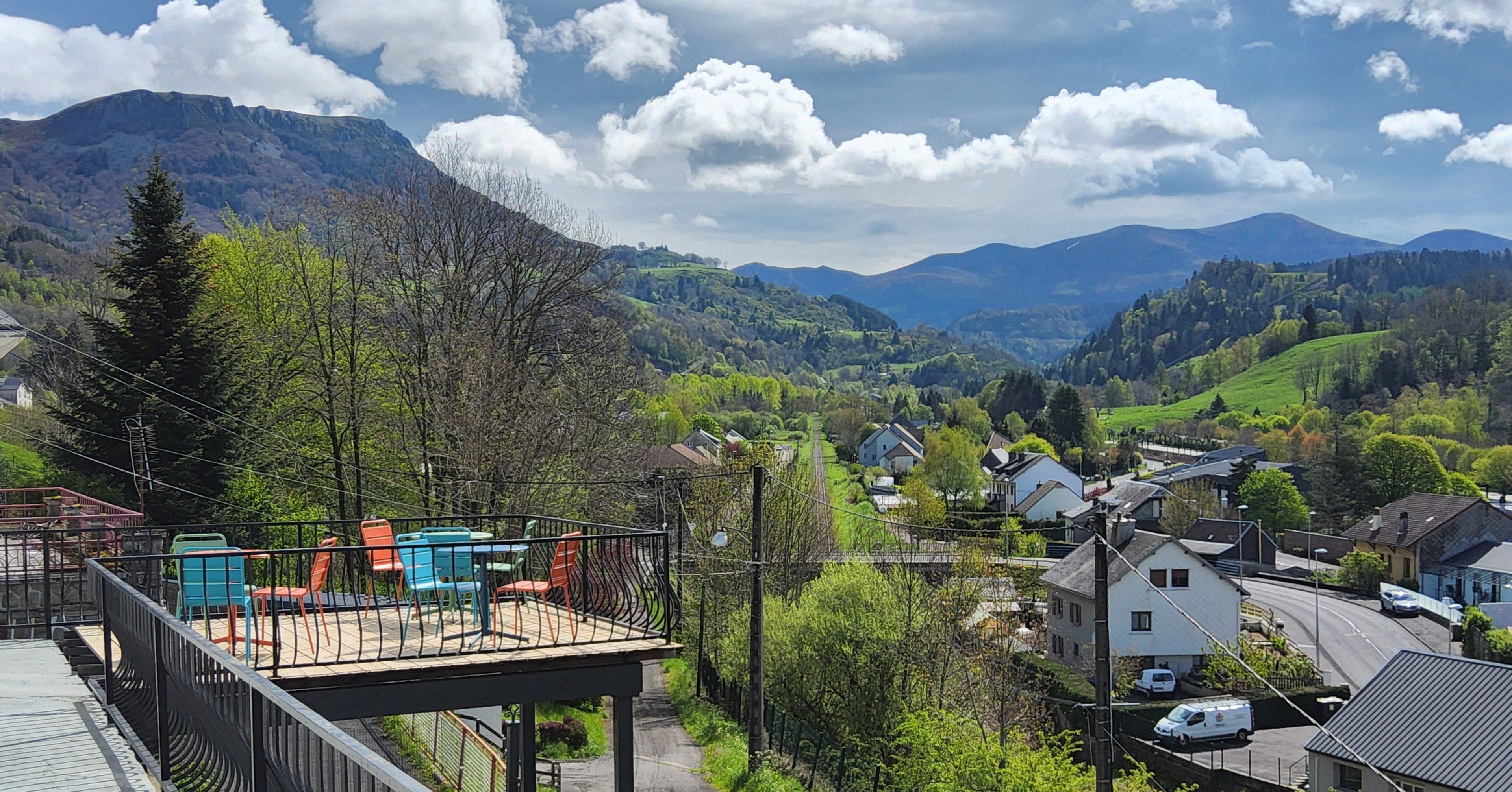 Une vue pittoresque d’un village avec des maisons, une voie ferrée et des montagnes en arrière-plan.