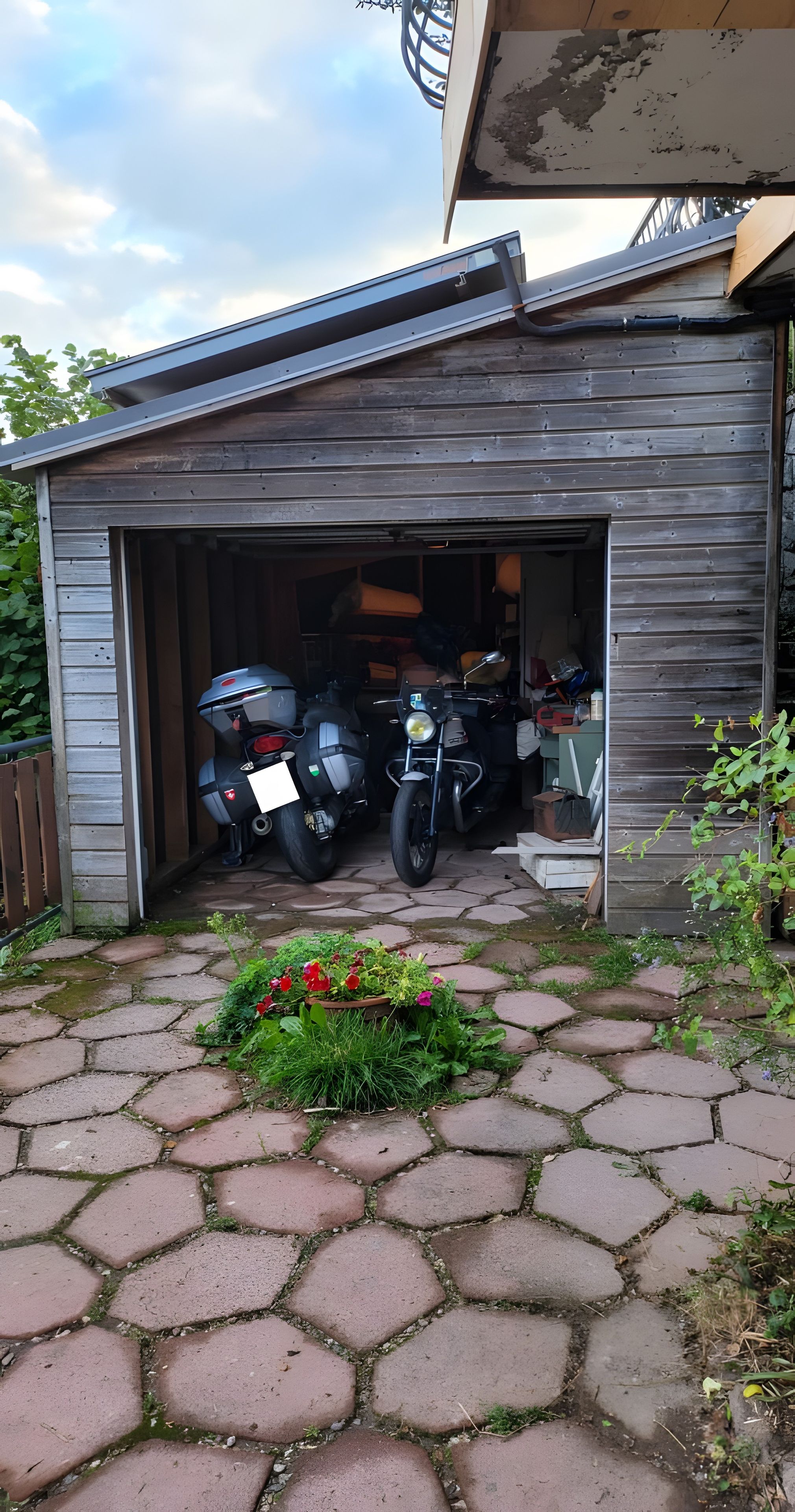 A garage with two motorcycles parked inside, a wooden exterior, and a stone-paved entrance.