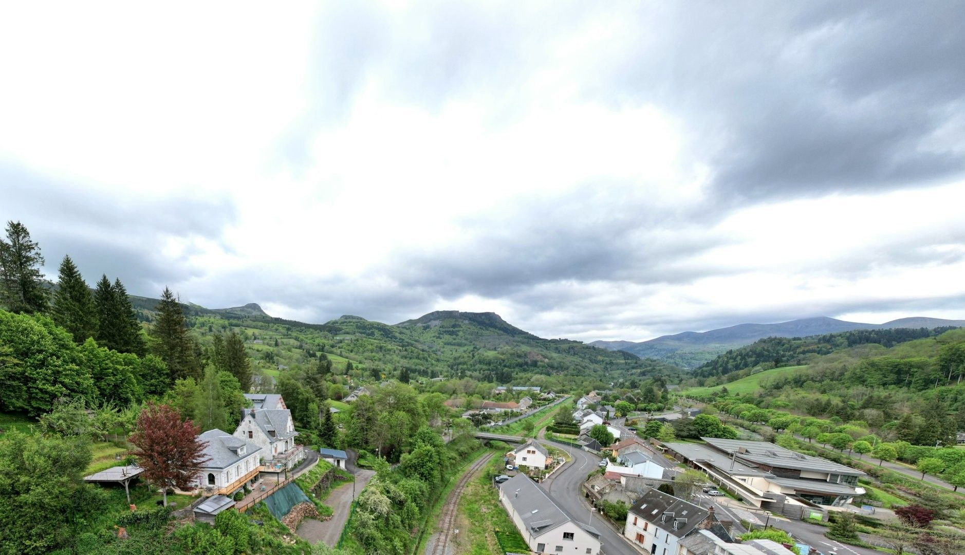Un paysage rural composé d’un mélange de bâtiments résidentiels, d’une route sinueuse et de collines douces en arrière-plan.