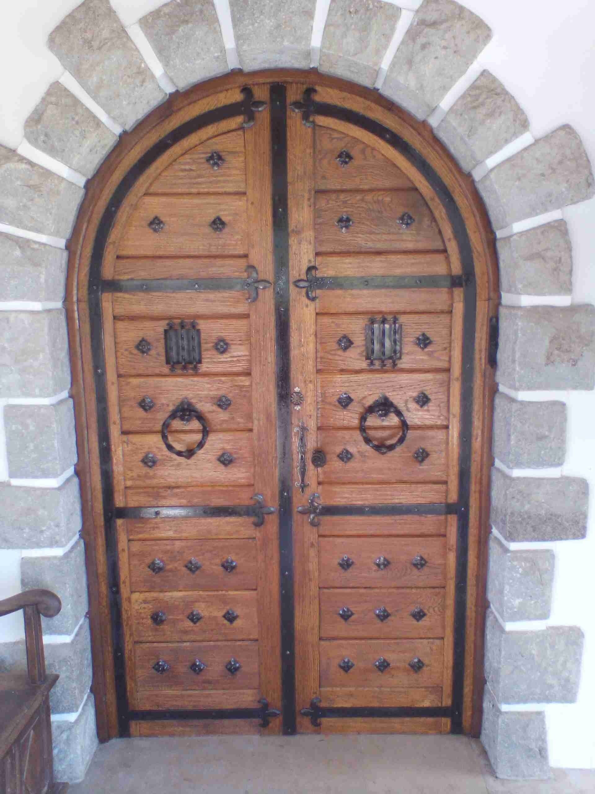 Unas amplias puertas dobles de madera con refuerzos metálicos, ubicadas en un arco de piedra.