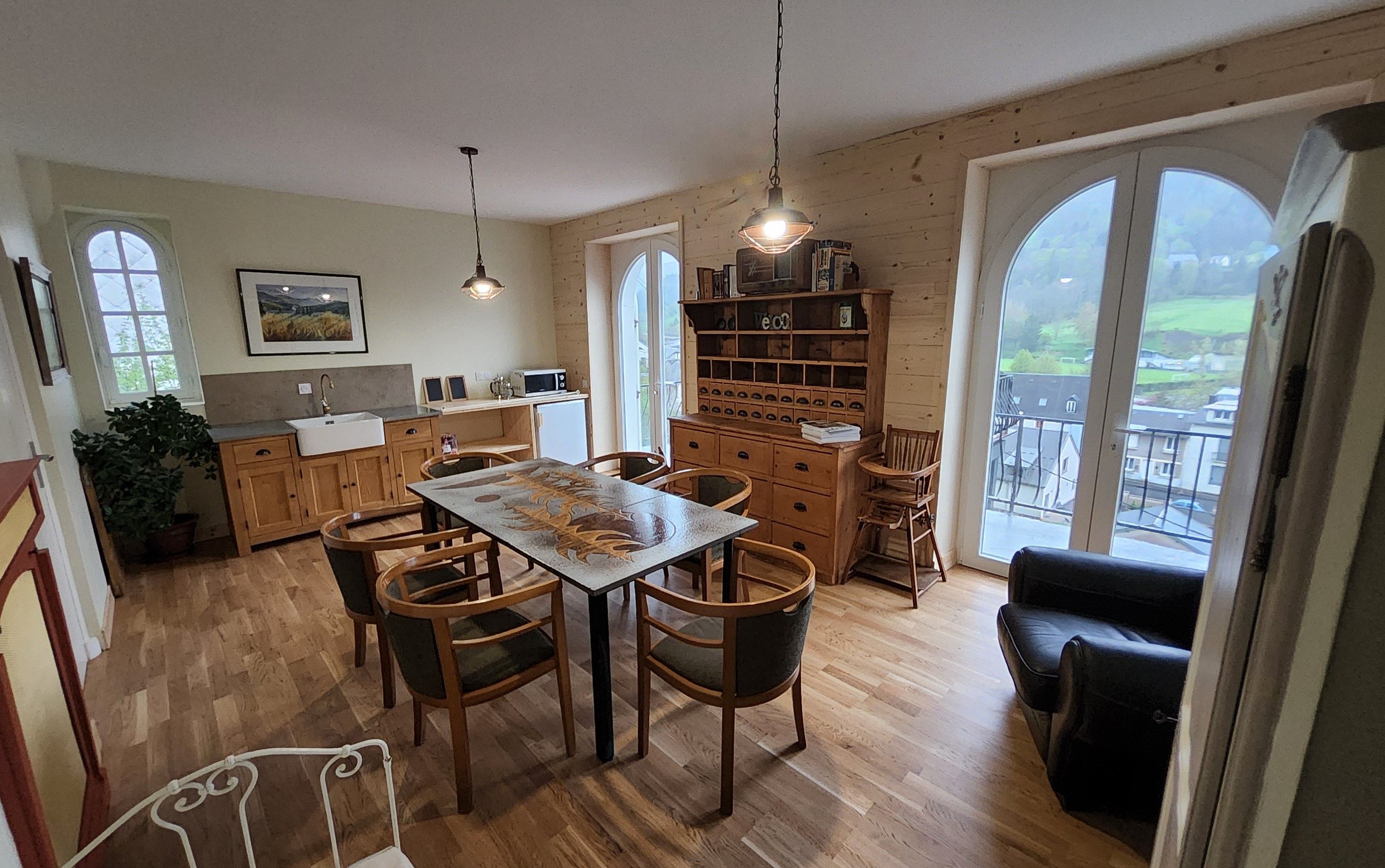 Een gezellige keuken met houten kasten, een eettafel en stoelen. Er is een groot raam met uitzicht op het platteland.
