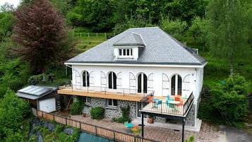 Une maison à deux étages avec un balcon, des fondations en pierre et un petit garage attenant.