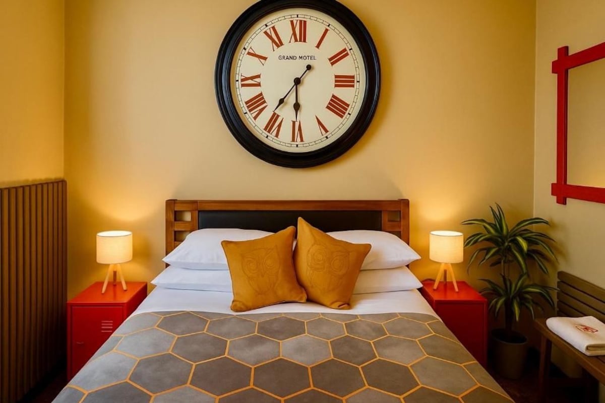 A hotel room with a bed, two bedside tables, a wall clock, and a mirror.