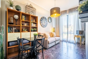 A living room with a sofa, chairs, a coffee table, a bookshelf, a TV, and a large window with curtains. - Bobotel  (Florence)