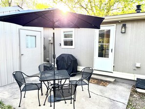 An outdoor patio with a table and chairs, a covered grill, and a door with a window. - Pet friendly 3-bedroom home 15 minutes from the stadiums! (Blue Springs)