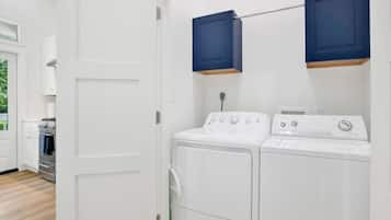 A laundry room with a washing machine and dryer, a white door, and a view into the kitchen area.