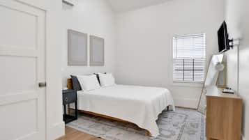 A bedroom with a bed, bedside table, lamp, and a window with blinds.