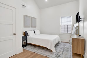 A bedroom with a bed, bedside table, lamp, and a window with blinds. - Sweet Caroline (Mobile)