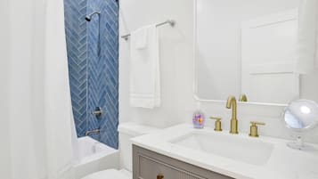 A bathroom with a white sink, gold faucets, a mirror, and a blue herringbone-patterned shower wall.