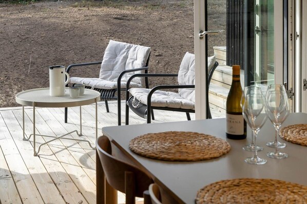Eine Holzterrasse mit Sitzgelegenheiten im Freien, einem Tisch mit gewebten Untersetzern, einer Weinflasche und Gläsern.