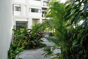 A modern building with multiple balconies and a lush garden area with various plants. - 1BR Condo Rooftop Pool & Gym Playa (Playa del Carmen)