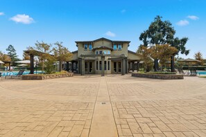 A two-story building with a central entrance, surrounded by a paved area with benches and a pool. - Spacious West Sac Retreat - Park, Patio & BBQ (West Sacramento)