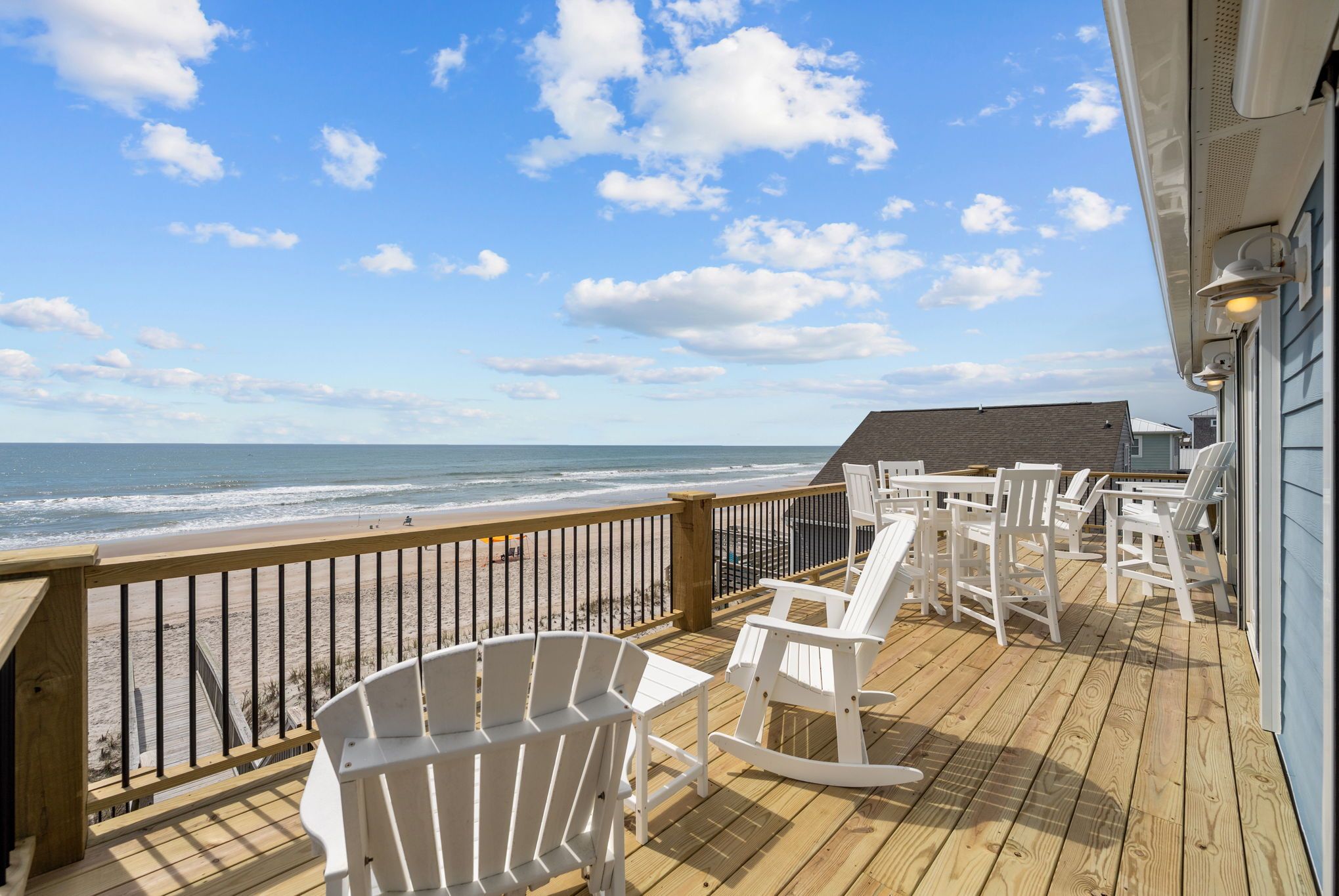 A wooden deck with white chairs and a table overlooking the beach.