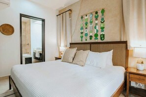Ein Hotelzimmer mit einem großen Bett, einem hölzernen Kopfteil, einem an der Wand befestigten Kunstwerk und einem durch eine offene Tür einsehbaren Badezimmer.