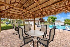 An outdoor patio with a thatched roof, seating area, and a pool. - Coastal Glam / Near Beach & Downtown / Heated Pool (Fort Myers)