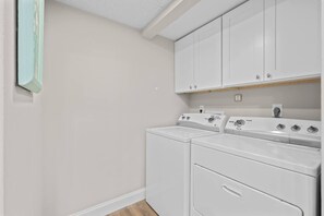 A laundry room with two washing machines and a dryer, white cabinets above, and a light switch on the wall. - Coastal Glam / Near Beach & Downtown / Heated Pool (Fort Myers)