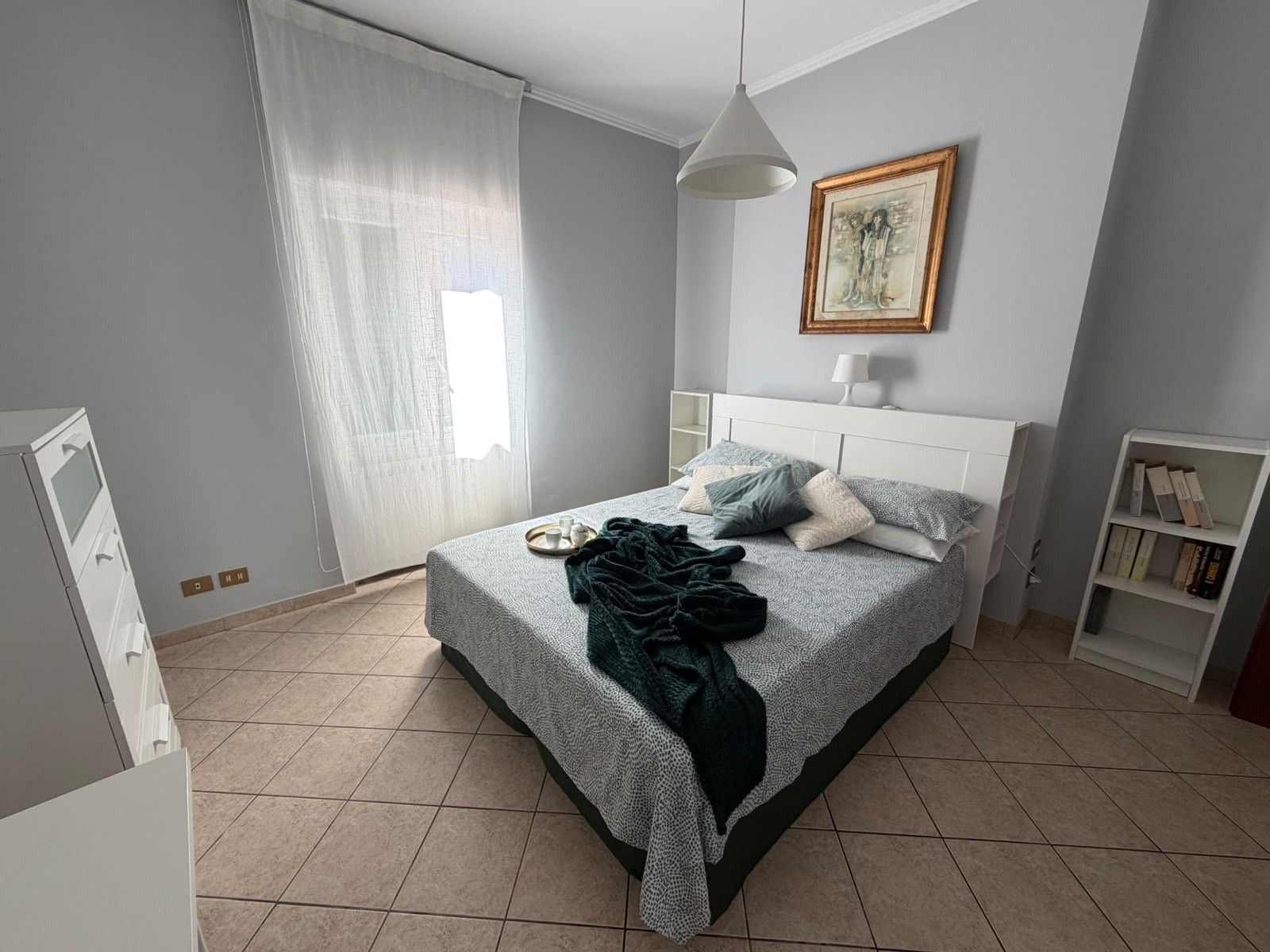 Una camera da letto ordinata con un letto, un comodino e una libreria.