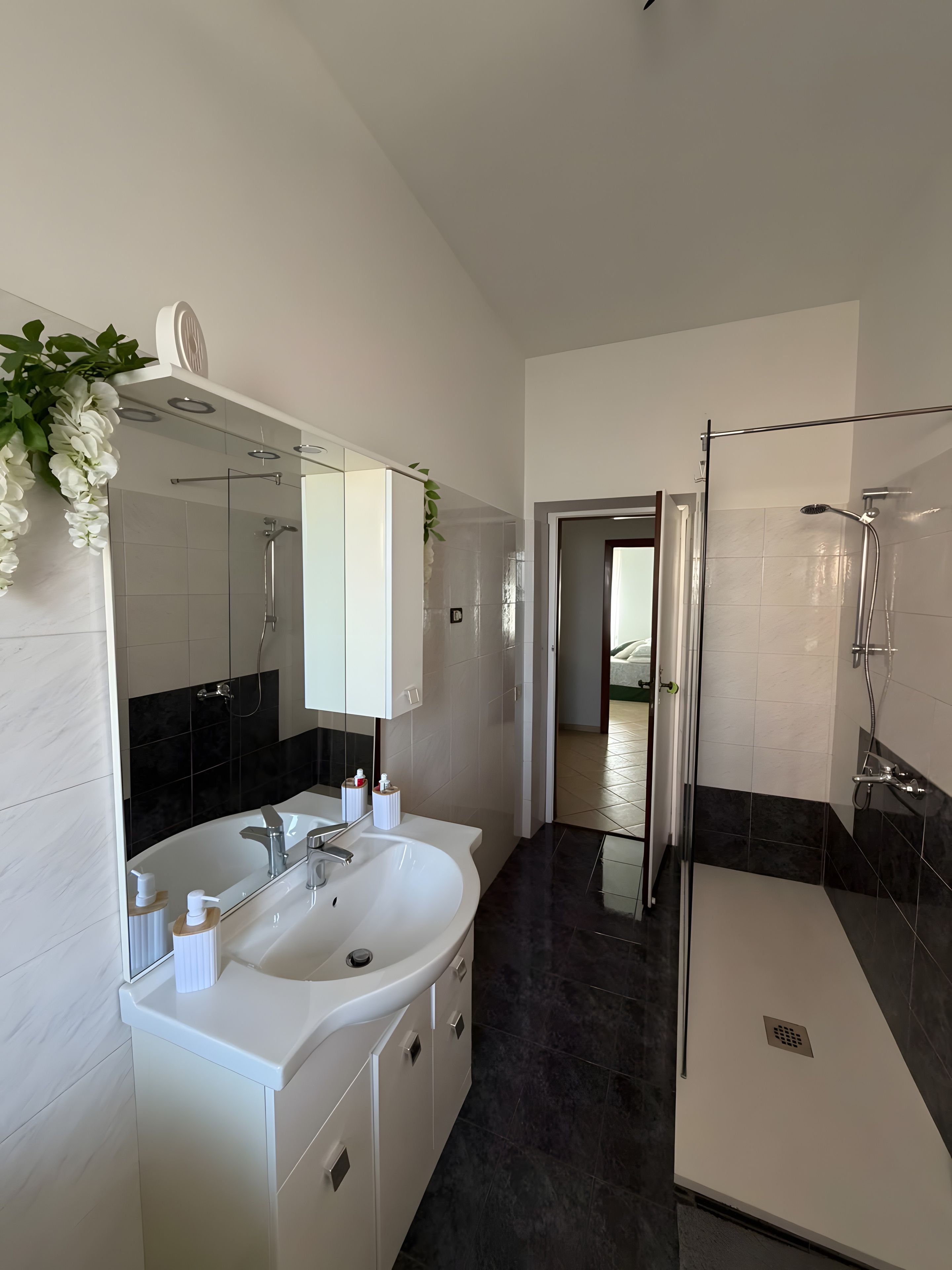 Un bagno moderno con un lavabo doppio, cabina doccia in vetro e una porta che dà su un'altra stanza.