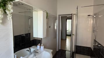 Un bagno moderno con un lavabo doppio, cabina doccia in vetro e una porta che dà su un'altra stanza.