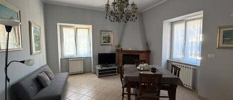 Uma sala de estar com sofá, mesa de jantar, cadeiras, lareira e lustre.