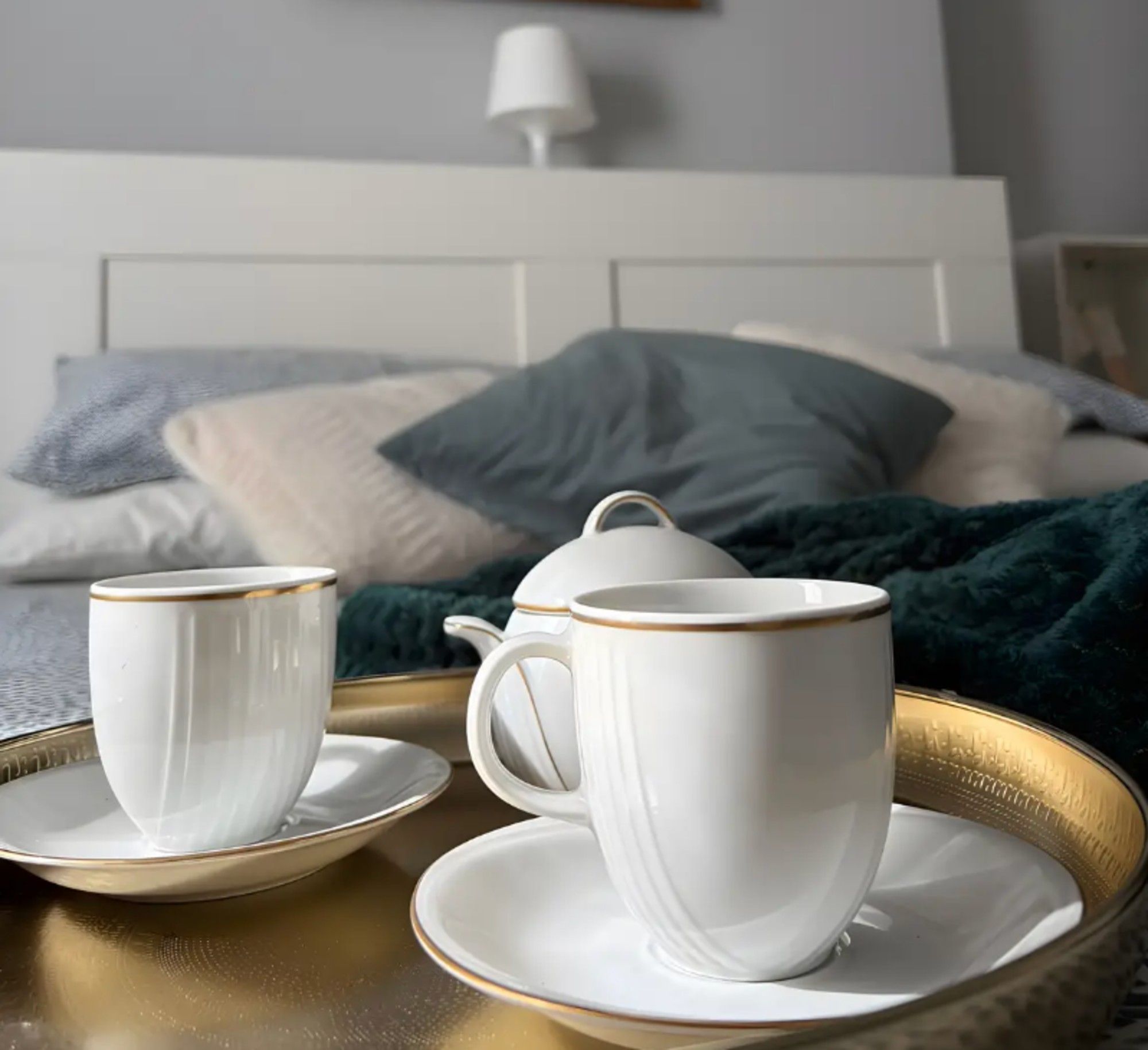 A bed with a white headboard, a bedside table with a lamp, and a green blanket.