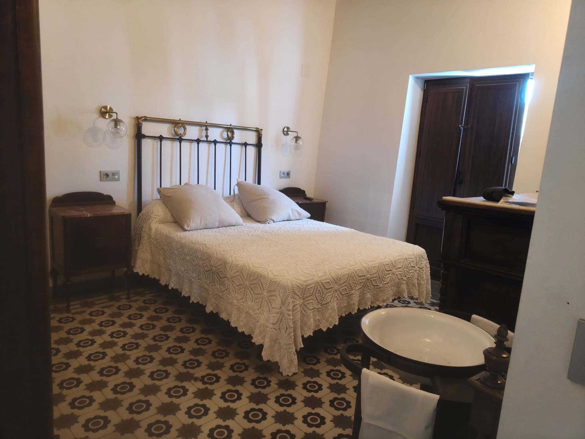 A bedroom with a bed, a nightstand, a dresser, a mirror, and a bathroom with a sink and toilet.