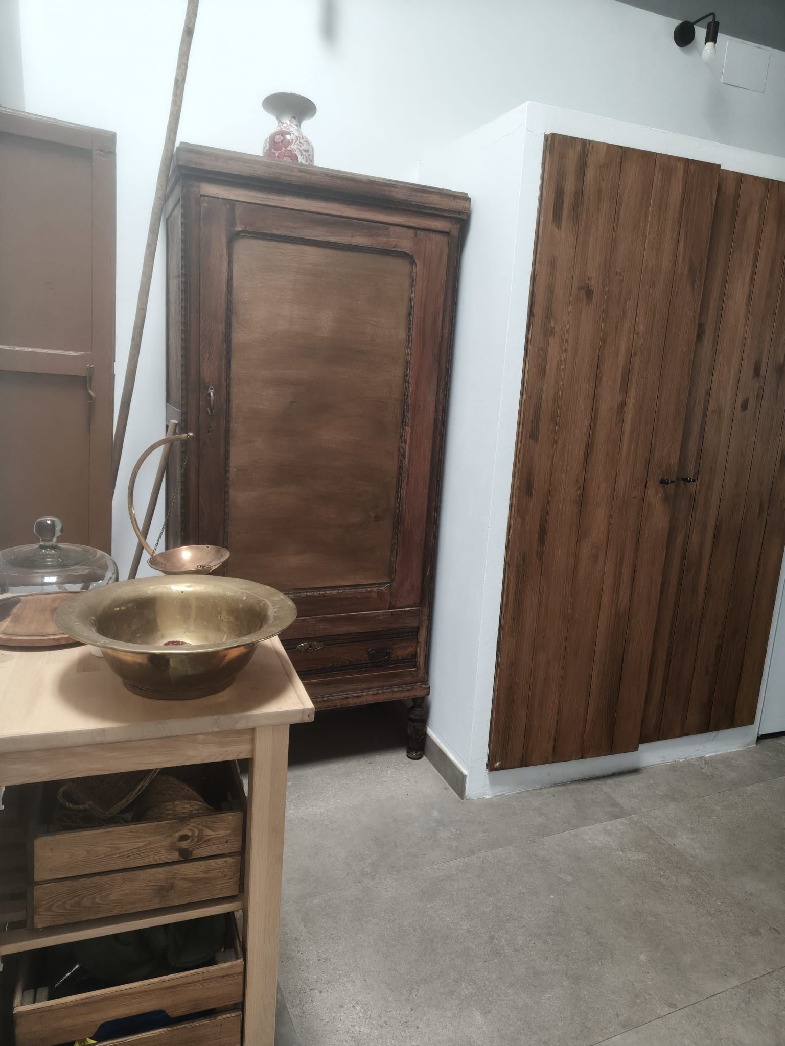 A room with a wooden cabinet, a metal bowl on a table, and a wardrobe.