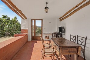 Zona de menjador rústica amb taula i cadires de fusta, taula rodona petita amb un ram i un televisor a la paret.