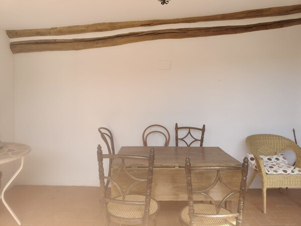 Een eetgedeelte met een houten tafel en stoelen, een rieten stoel en een klein tafeltje met een witte tafelkleed.