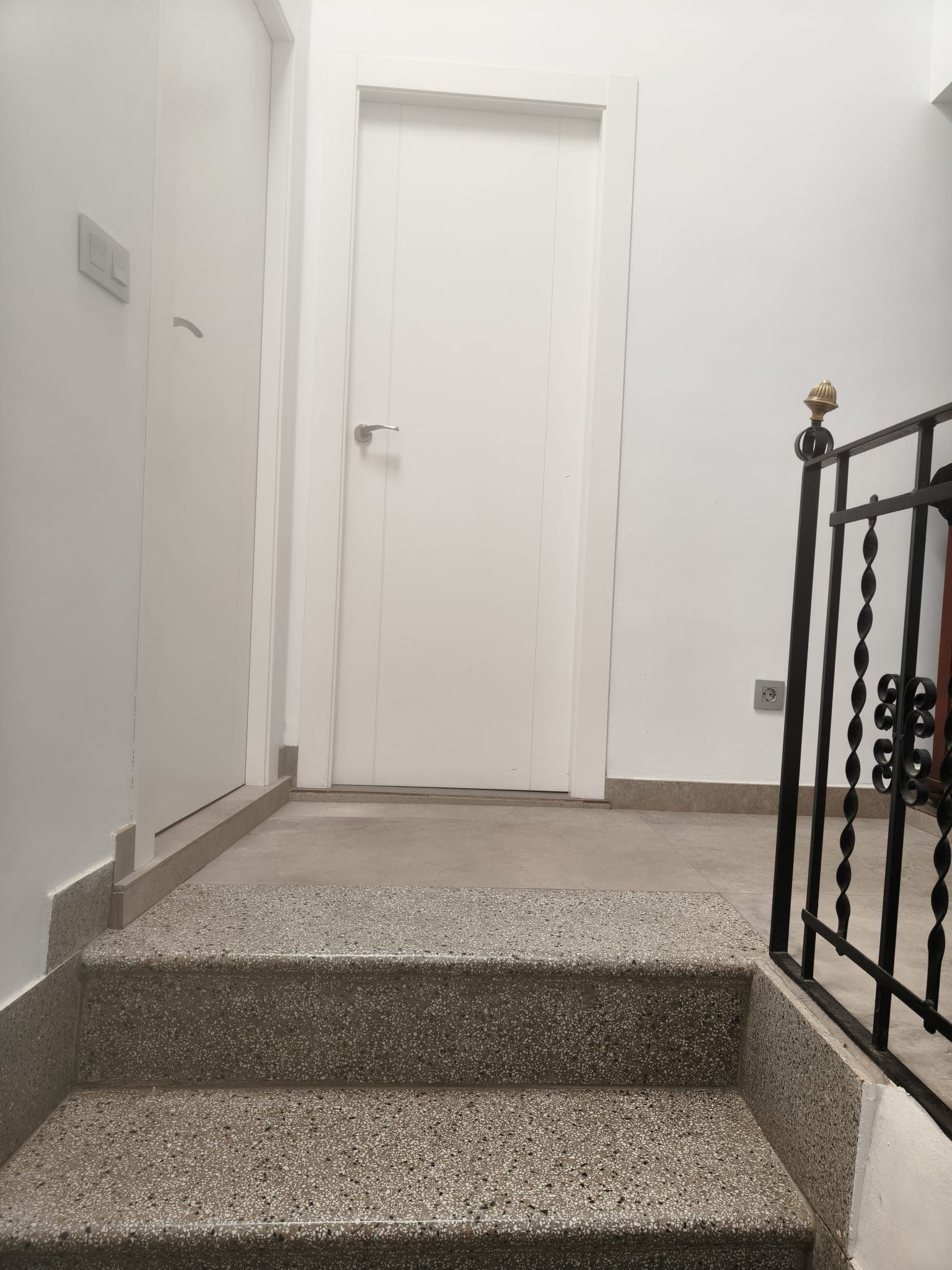 A staircase leading to a white door, with a metal railing on the right.