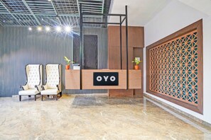 Un mostrador de recepción con un letrero, dos sillones tapizados, una pared decorativa y un separador con diseño.