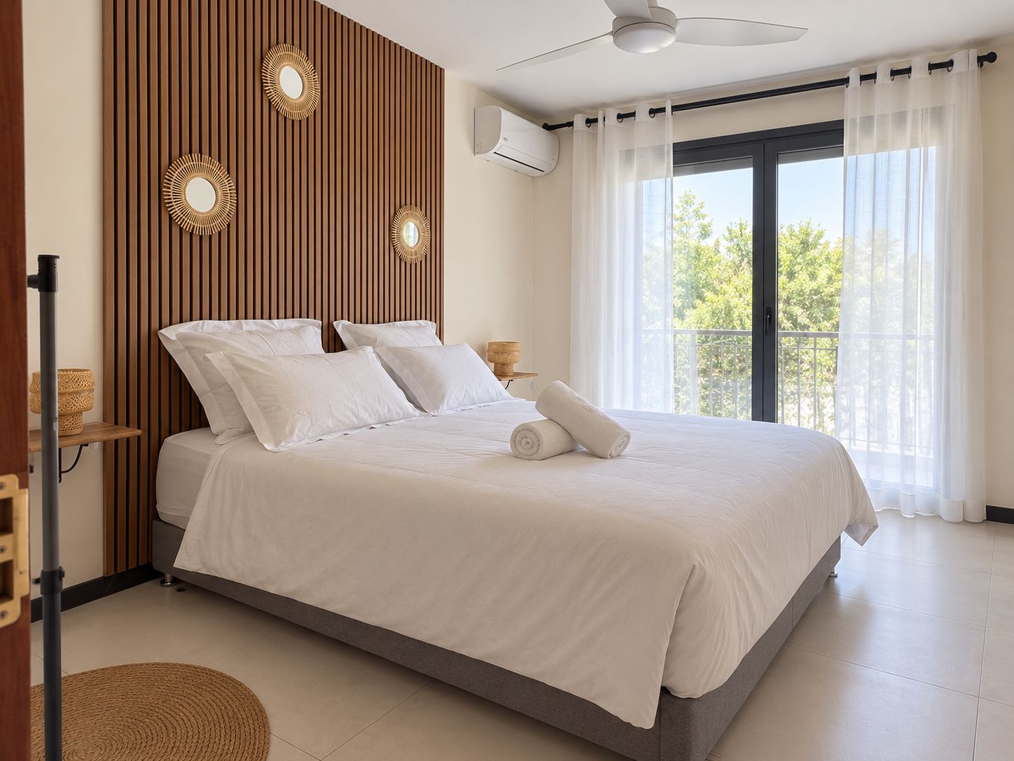 Une chambre à coucher comprenant un lit, un ventilateur de plafond, une fenêtre avec des rideaux et un climatiseur fixé au mur.