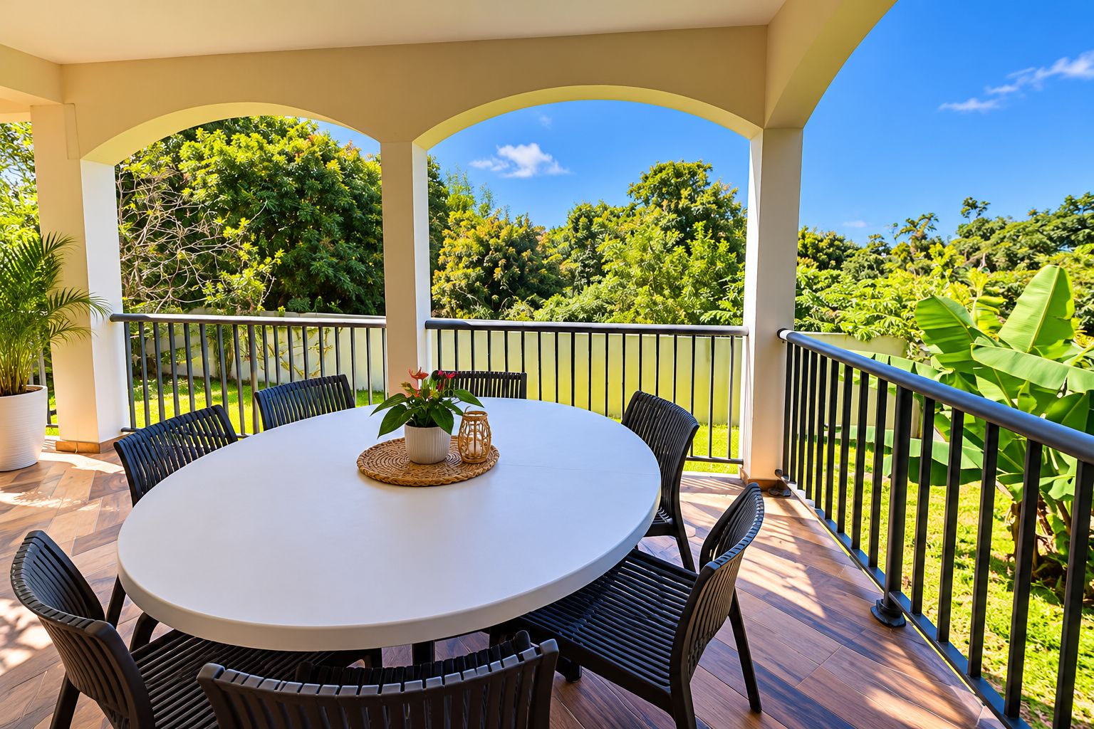 Un espace extérieur abrité, doté d’une table ronde et de chaises, entouré d’une balustrade et offrant une vue sur un paysage verdoyant luxuriant.