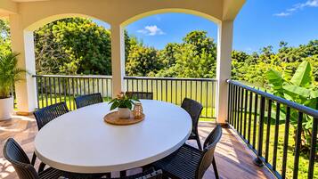 Un espace extérieur abrité, doté d’une table ronde et de chaises, entouré d’une balustrade et offrant une vue sur un paysage verdoyant luxuriant.