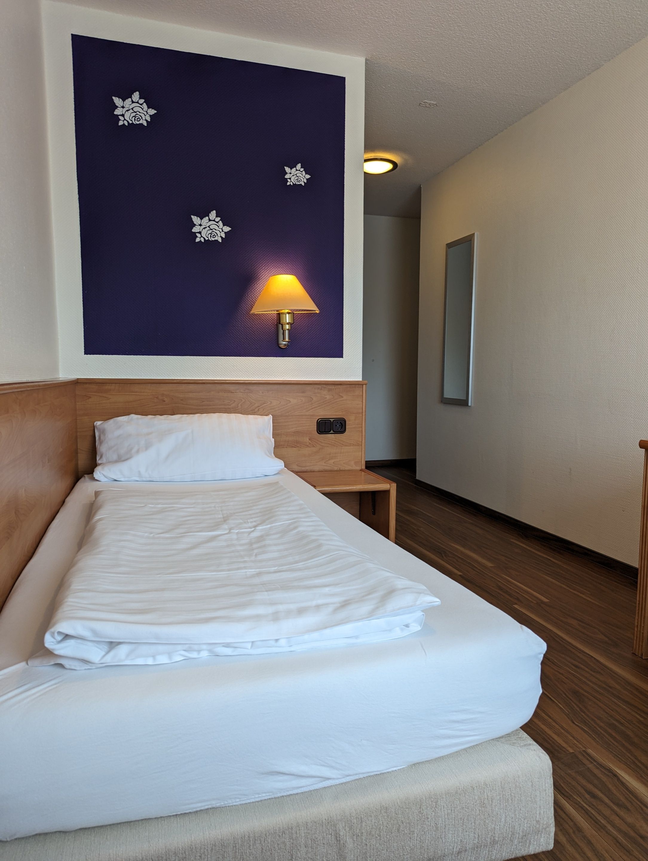 Una habitación de hotel con una cama, una mesita de noche, una lámpara de pared y un espejo.